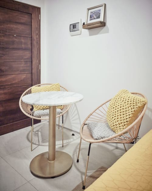 Habitación moderna en Pares Homes CDMX con sillas de ratán tejido, mesa redonda de mármol y puerta de madera oscura