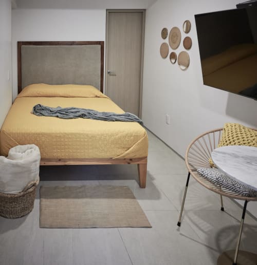 Dormitorio moderno en Pares Homes Ciudad de México con ropa de cama amarilla, silla tejida, arte mural y TV de pantalla plana