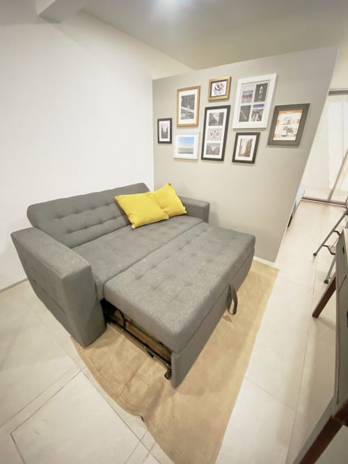 Sofá cama gris con cojines amarillos en departamento moderno de CDMX en Pares Homes, con pared de galería de arte