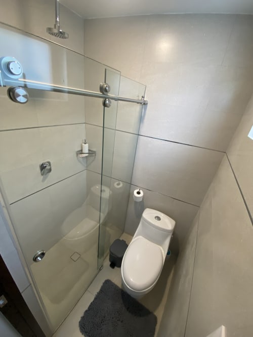 Baño moderno con ducha de cristal, inodoro blanco y paredes alicatadas en apartamento Pares Homes de la Ciudad de México