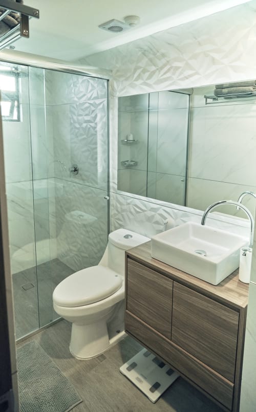 Baño moderno en apartamento Pares Homes en CDMX con ducha de vidrio, lavamanos blanco tipo vasija y vanidor de madera.