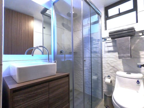 Baño moderno en apartamento de Pares Homes en CDMX con ducha de vidrio, lavabo de cerámica blanca y azulejos de mármol