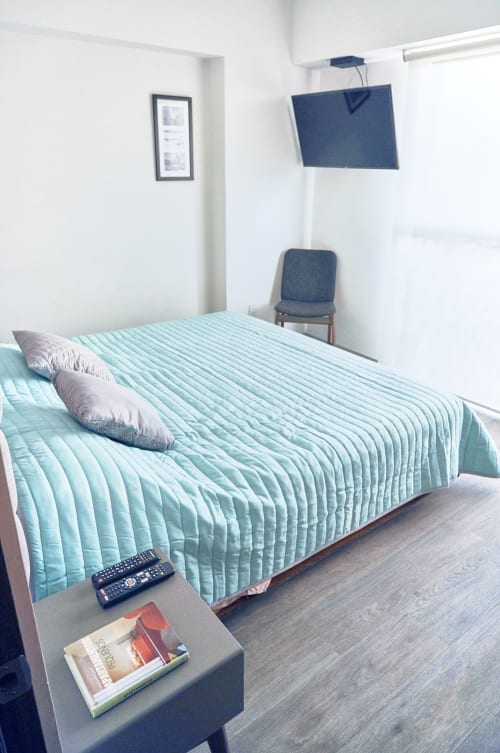 Moderno dormitorio en apartamento Pares Homes CDMX con ropa de cama turquesa, TV montada en pared y decoración minimalista