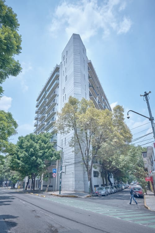 Edificio moderno de apartamentos en la Ciudad de México con vistas urbanas, ubicado en esquina con autos estacionados y árboles verdes