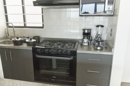 Cocina moderna en apartamento de CDMX en Pares Homes con estufa de gas, encimera de granito, electrodomésticos de acero inoxidable y vista a la ciudad.