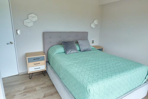 Recámara moderna en apartamento de Pares Homes CDMX con ropa de cama verde menta, cabecera gris y buró de madera