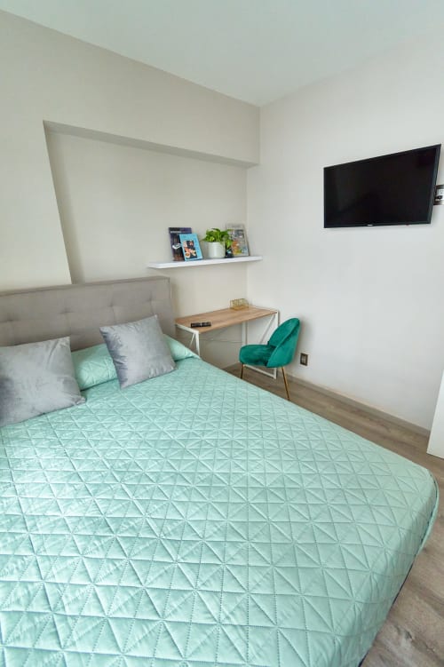 Recámara moderna en departamento de Pares Homes Ciudad de México con ropa de cama verde menta, cabecera gris, TV mural y detalles turquesa