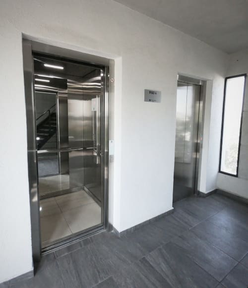 Moderno vestíbulo de ascensor en apartamentos Pares Homes, Ciudad de México, con puertas de acero inoxidable y señalización de piso 6