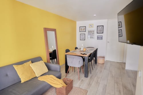 Apartamento moderno en CDMX de Pares Homes con pared acentuada en amarillo, sofá gris, mesa de comedor y obras de arte enmarcadas