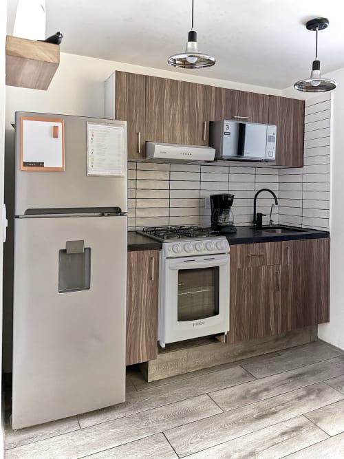 Cocina moderna en apartamento de Pares Homes en CDMX con gabinetes de madera, electrodomésticos de acero inoxidable y encimeras negras