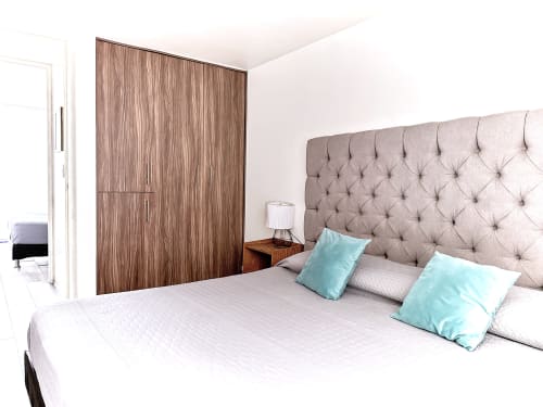 Recámara moderna en apartamento Pares Homes, CDMX, con cabecera capitonada, guardarropa de madera y almohadas turquesas