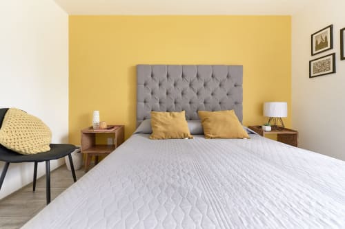 Dormitorio moderno en Pares Homes CDMX con pared acentuada en amarillo, cabecero capitonado gris y almohadas doradas