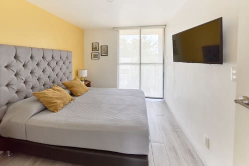 Recámara moderna en Pares Homes Ciudad de México con cabecera capitonada gris, detalles en amarillo y TV montado en pared