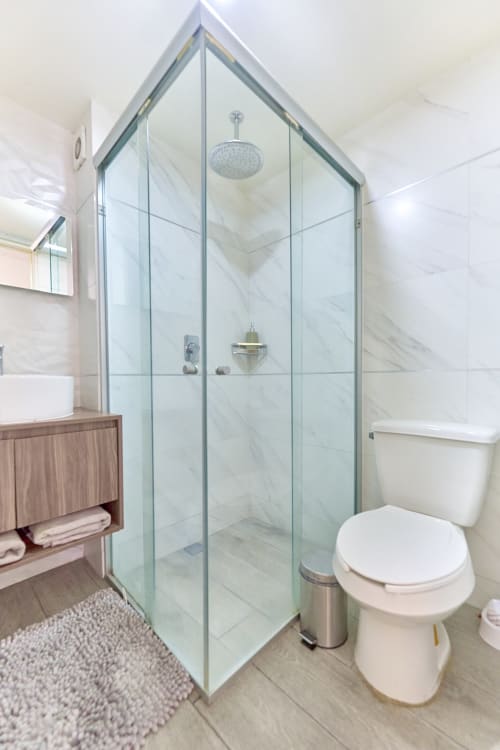 Baño moderno en apartamento de Pares Homes en la Ciudad de México con ducha de mármol, vanidad flotante e inodoro blanco