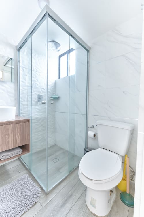 Baño moderno del departamento Pares Homes en CDMX con ducha de cristal, inodoro blanco y vanidad de madera.
