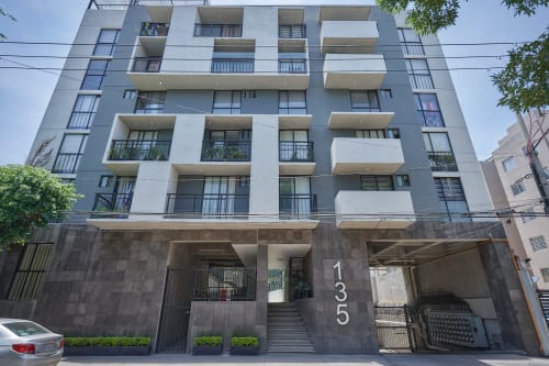 Moderno edificio de apartamentos Pares Homes en CDMX con fachada gris y blanca, balcones y entrada a nivel de calle.