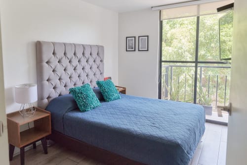 Habitación moderna en departamento Pares Homes CDMX con cabecera capitonada, ropa de cama azul y balcón con vista al verde