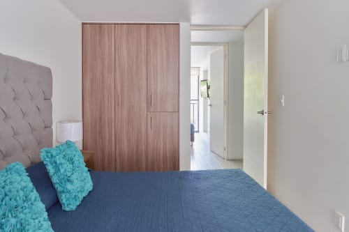 Dormitorio moderno en apartamento Pares Homes Ciudad de México con almohadas turquesas, ropa de cama acolchada azul, cabecera gris y madera