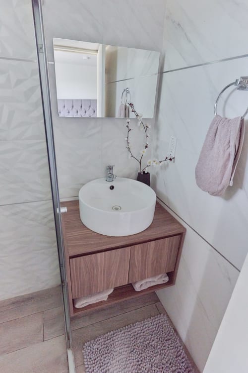 Baño moderno del apartamento Pares Homes en CDMX con lavabo redondo blanco, tocador de madera y paredes alicatadas
