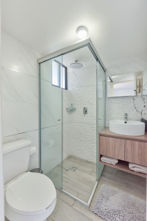 Baño moderno de Pares Homes CDMX con cabina de ducha de cristal, lavamanos blanco y azulejos de mármol