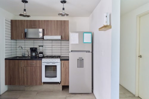 Moderna cocina compacta en apartamento de Pares Homes, Ciudad de México, con gabinetes de madera, refrigerador de acero inoxidable y blanco
