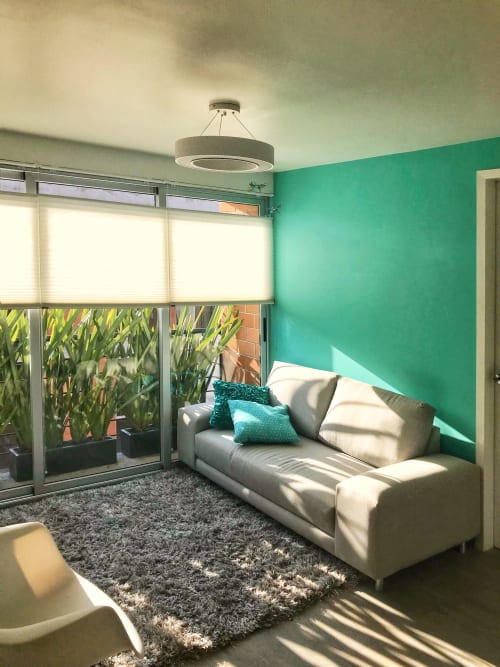 Luminosa sala de estar moderna en Pares Homes CDMX con paredes turquesas, sofá crema, grandes ventanales y luz natural