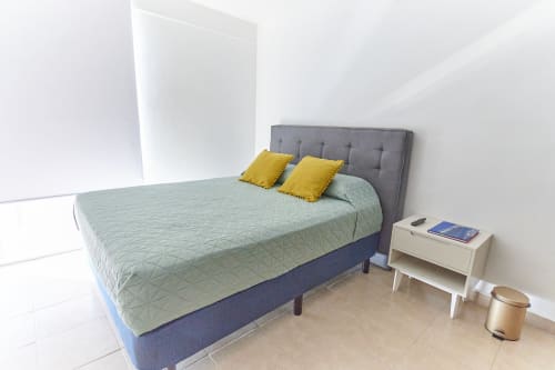 Moderno dormitorio en apartamento Pares Homes, CDMX con cama queen, cabecero gris, almohadas amarillas y mesita minimalista