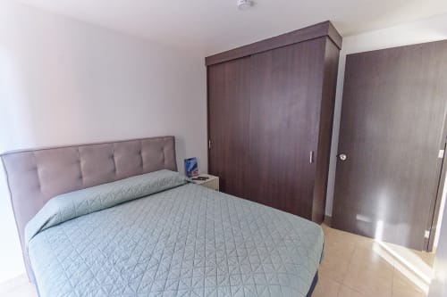 Recámara moderna en apartamento Pares Homes CDMX con cama queen, cabecera acolchada y roperos de madera oscura.