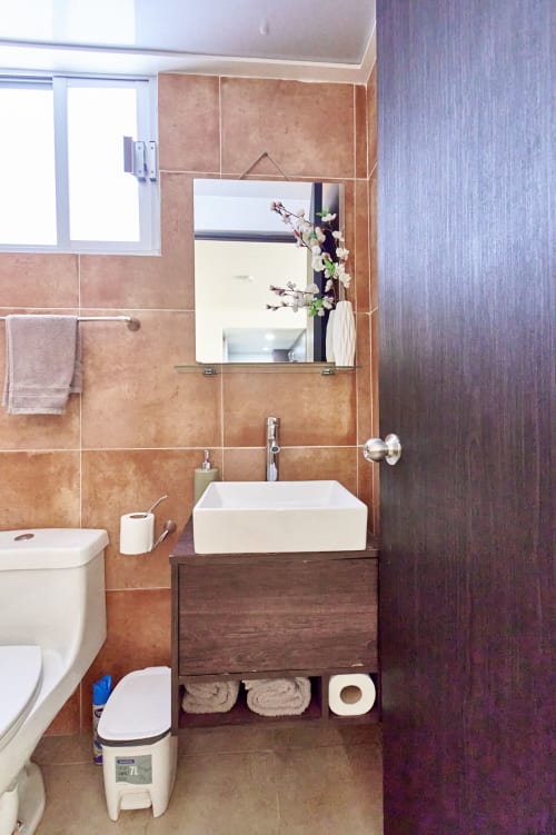 Baño moderno en apartamento Pares Homes, CDMX con azulejos de terracota, lavabo tipo recipiente y tocador flotante.