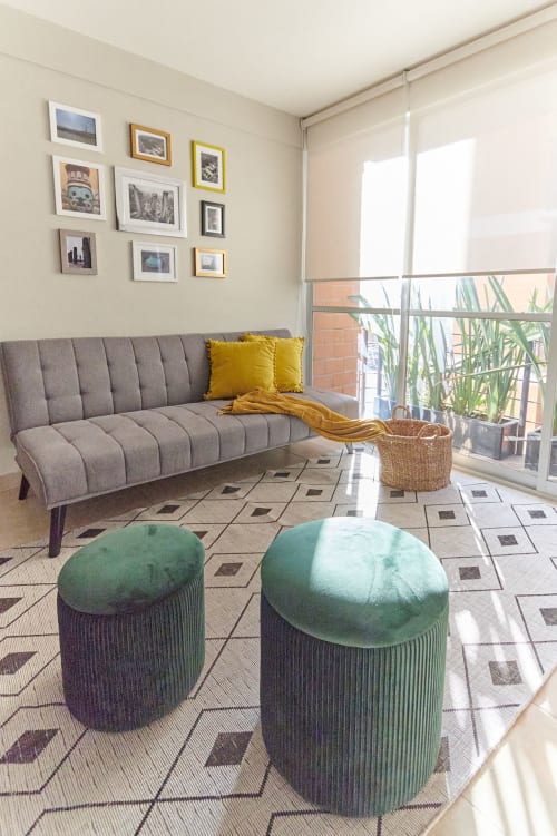 Sala moderna en CDMX con sofá gris, otomanas verdes, galería de arte y balcón con vista a edificios de ladrillo