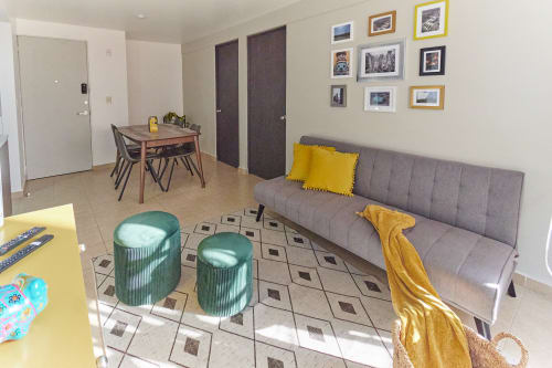 Sala moderna de departamento en CDMX con sofá gris, acentos amarillos, mesa de comedor y galería de arte en Pares Homes