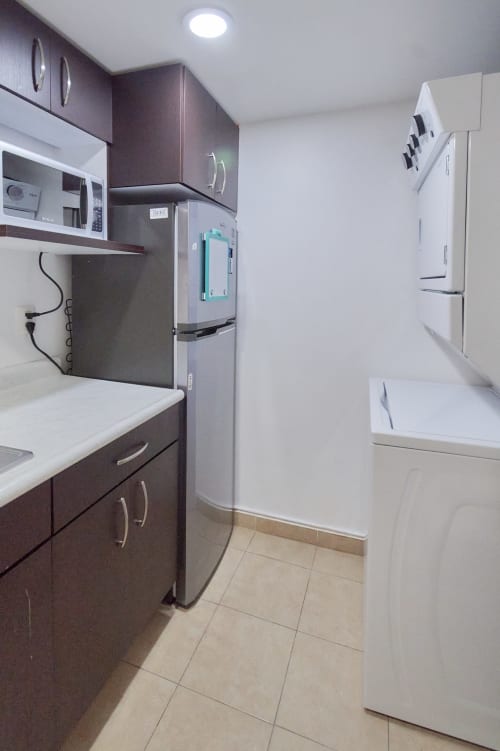 Cocina moderna con gabinetes oscuros, refrigerador de acero inoxidable y electrodomésticos blancos en apartamento Pares Homes, Ciudad de México