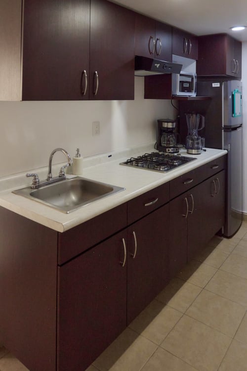 Cocina moderna en apartamento Pares Homes CDMX con gabinetes oscuros, encimera blanca, electrodomésticos acero inoxidable y estufa gas