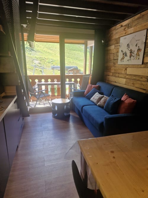 Canapé bleu avec vue montagne sur balcon dans le salon de l'appartement CMD Méribel Le Pralin, murs en bois