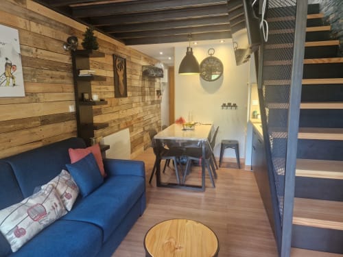 Séjour moderne du CMD Méribel Le Pralin avec canapé bleu, murs en bois, table à manger et accès par escalier.
