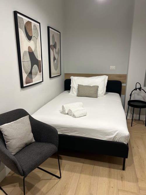 Camera moderna a Casa Lounge Istria Cagliari con letto nero, biancheria bianca, sedia grigia e arte astratta a muro