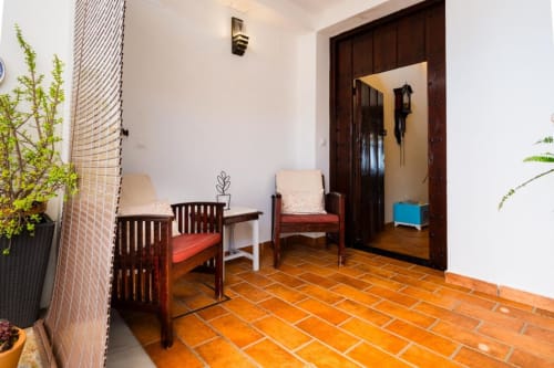 Entrada luminosa con piso de barro cocido en Villas Vacacionales Sevilla en Salteras, con sillas de madera y puerta de madera oscura