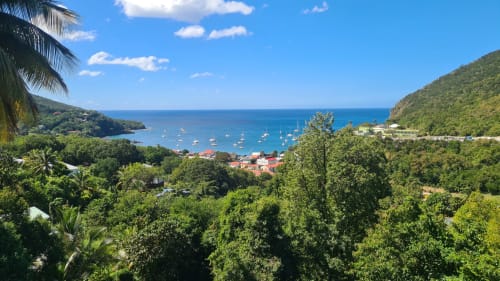 Baie tropicale des Hauts de Deshaies avec voiliers, végétation luxuriante et bâtiments aux toits rouges dominant les eaux turquoise des Caraïbes