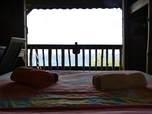 Chambre de villa vue mer aux Hauts De Deshaies avec serviettes roulées sur le lit et balcon donnant sur l'océan