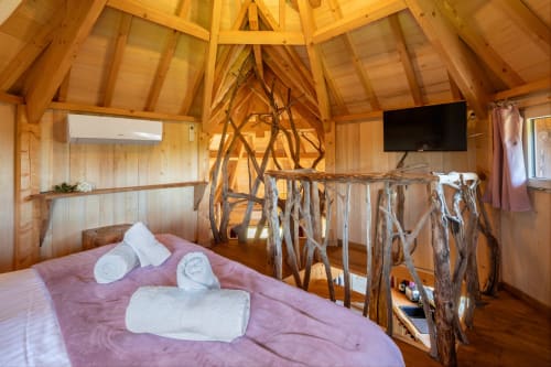 Rustieke houten slaapkamer met roze beddengoed, drijfhout reling en gewelfd plafond in Domaine De Campagnac in Carsac-Aillac
