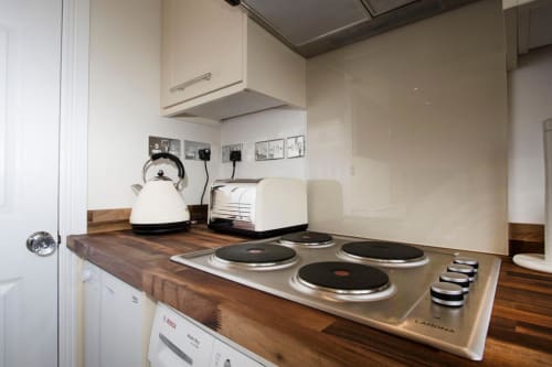 Compact kitchen at Grapevine Studio in Waterbeach, Cambridge with electric cooktop, kettle, and toaster on wooden countertop
