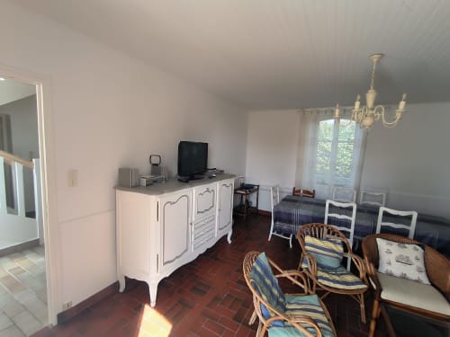 Charmant séjour avec mobilier blanc, télévision, chaises en rotin et vue sur le jardin à Locmaria Belle Île en Mer