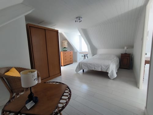 Chambre lumineuse avec murs blancs, armoire en bois, lit et coin salon dans un gîte de Belle Île en Mer