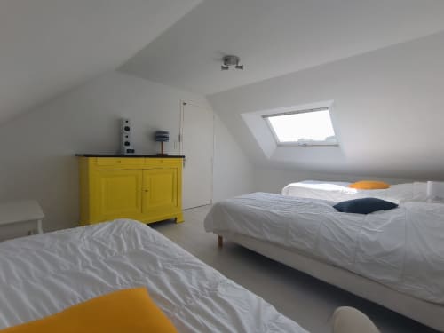 Chambre lumineuse sous les toits avec deux lits blancs, commode jaune et lucarne à la Maison Locmaria, Belle Île en Mer