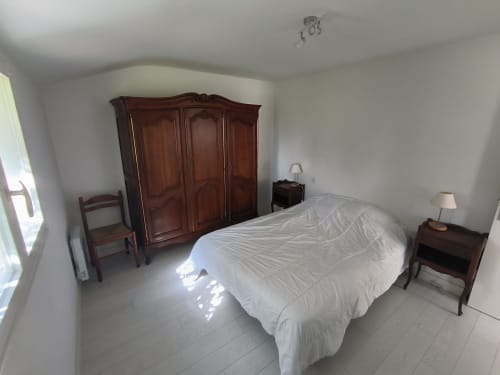 Chambre spacieuse du gîte Belle-Île-en-Mer avec armoire en bois, lit, tables de nuit et vue sur le jardin