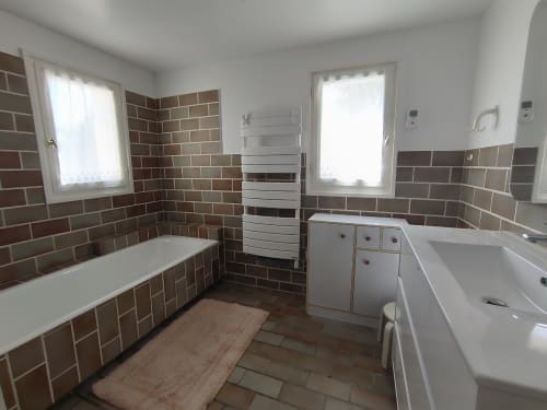 Salle de bains spacieuse avec carrelage en briques brunes, doubles vasques, baignoire, sèche-serviettes chauffant et grandes fenêtres à Belle-Île-en-Mer