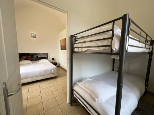 Metal bunk bed with white linens in Locacharme cottage La Chocolaterie, Blois, with bedroom visible through doorway