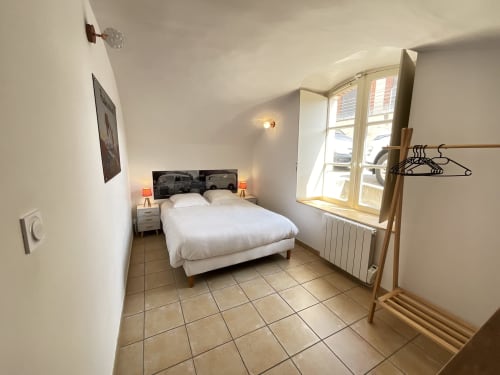 Bright bedroom at Locacharme Gîte La Chocolaterie in Blois with white bed, garden view windows, and wooden clothing rack