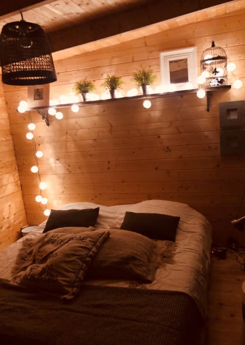 Chambre cosy en bois à la ADELOUANE BnB à Aigues-mortes avec guirlandes lumineuses, suspension noire et cage à oiseaux décorativ