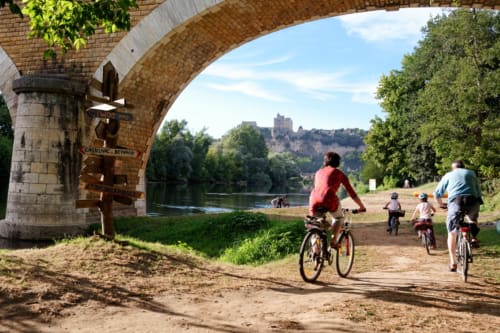 Cyclists riding under historic stone bridge near Domaine De Campagnac in Dordogne, France